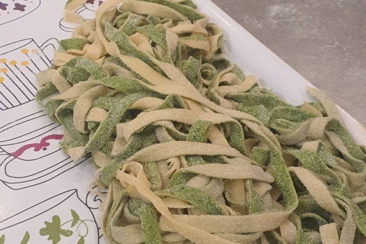 Homemade spinach and regular pasta on a plate near a rolling pin.
