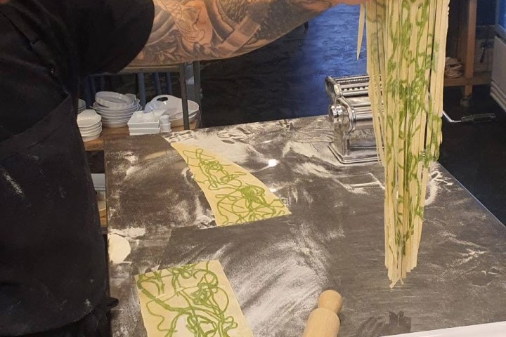 Chef stretching fresh pasta dough in a kitchen.