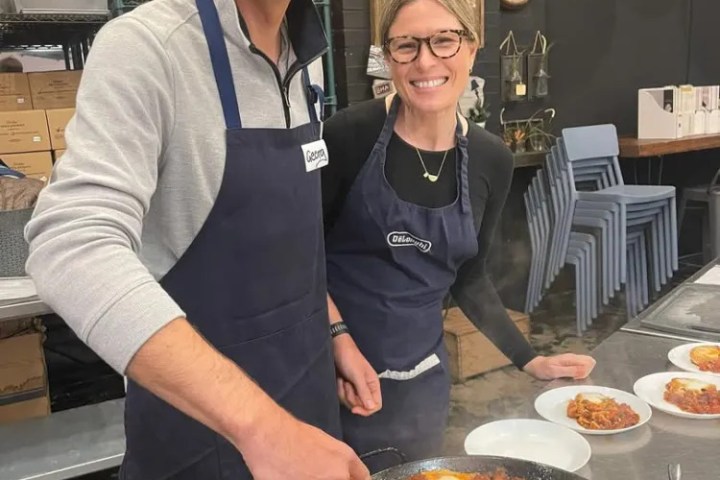 Two people smiling, cooking together with aprons in a kitchen, preparing food in a large pan.