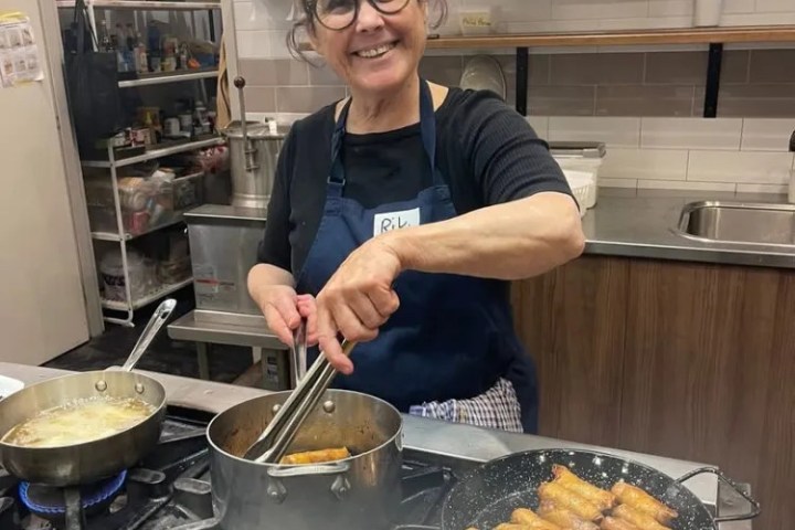 Woman in apron frying food in kitchen with smile.
