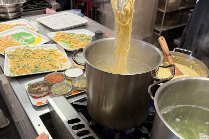Chef lifting noodles from boiling pot in a busy kitchen.