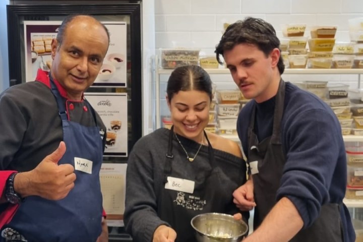 Three people cooking together, adding garnish to a dish in a kitchen setting.