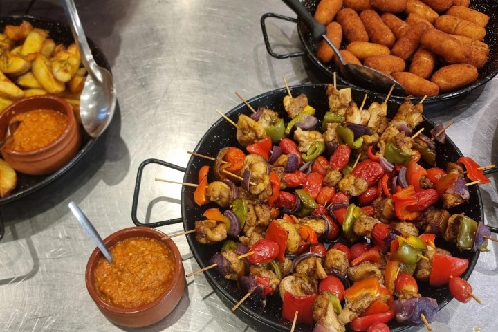 Dishes of potatoes, skewers, croquettes, and sauce on a table.