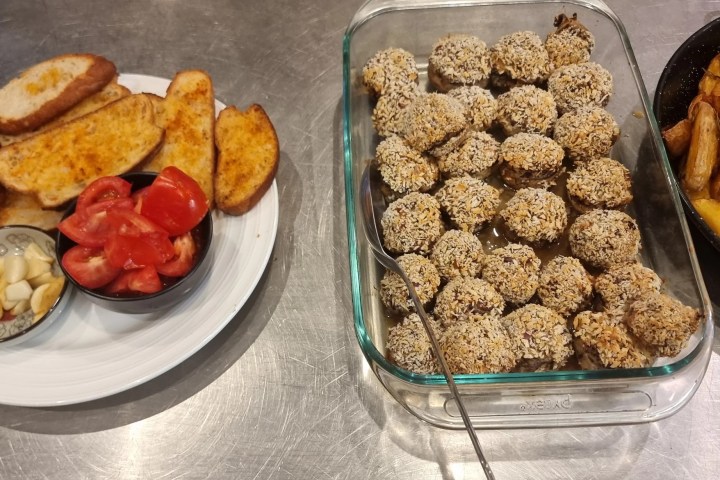 Plates of garlic bread, tomato and garlic, coated balls, and potato wedges on a metal surface.