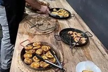 Person serving food from various pans on a wooden table.