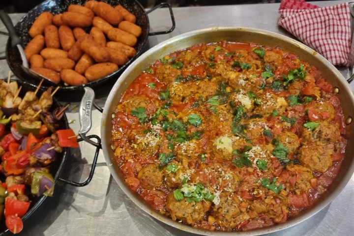 Three dishes: skewered vegetables, fried croquettes, and meatballs in tomato sauce on a metal surface.