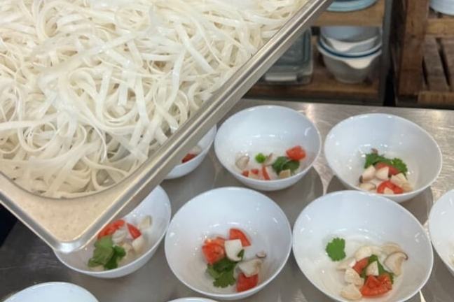 Tray of rice noodles above white bowls with vegetables and herbs.