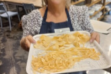 Person holding a tray of uncooked pasta in a kitchen setting.