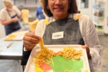 Woman in apron holding a tray of fresh pasta in a kitchen setting.