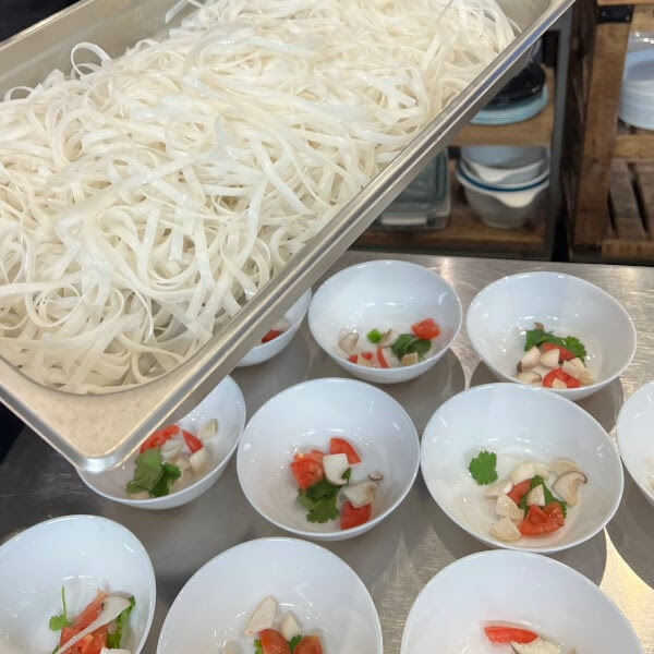 Tray of rice noodles above bowls with herbs and vegetables on a table.