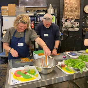 Two people preparing food on a kitchen counter with vegetables.