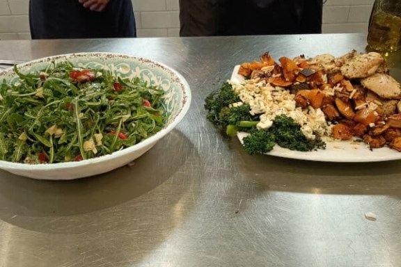 Two plates on a table: salad with arugula and mixed vegetables and a platter with roasted vegetables and chicken.