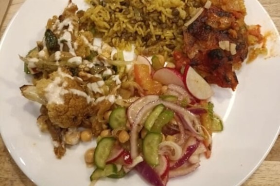 Plate with rice, roasted vegetables, salad, and grilled meat on wooden table.