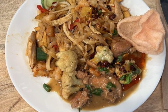 Plate of stir-fried noodles with vegetables, meat, and shrimp on a wooden table.