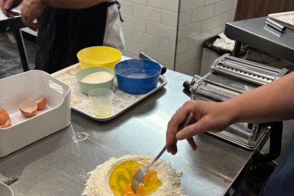 Person mixing egg and flour on a metal counter with a pasta maker nearby.