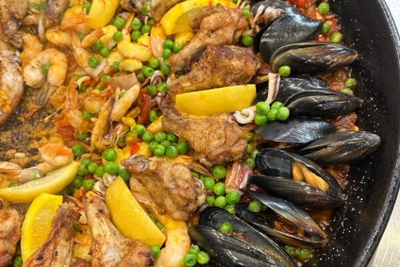 A pan of paella with mussels, chicken, shrimp, lemon wedges, and green peas.