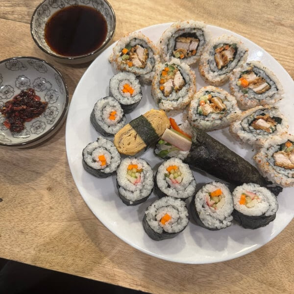 Plate of sushi rolls with soy sauce and chili sauce on a wooden table.