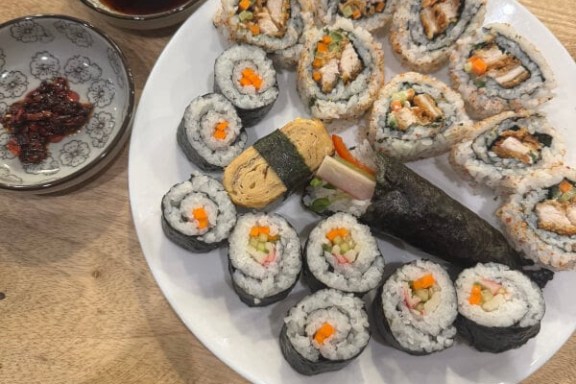 Plate of sushi rolls with soy sauce and chili sauce on a wooden table.