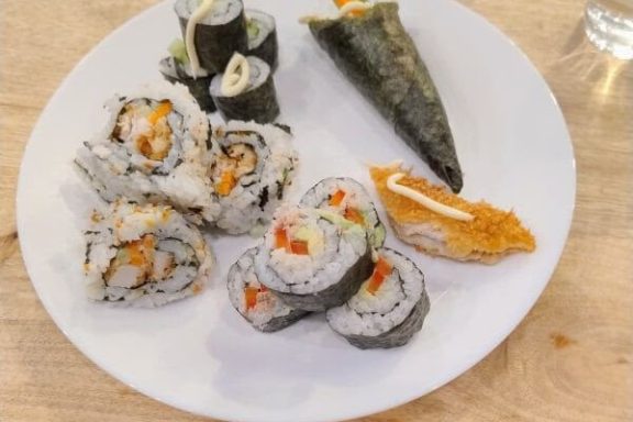 Plate of assorted sushi rolls and hand roll on a wooden table.