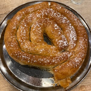 Coiled pastry with powdered sugar on a metal tray, partially eaten.