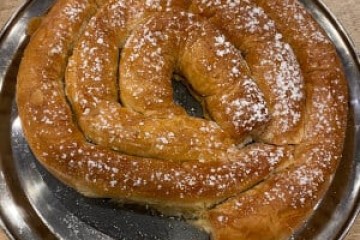 Coiled pastry with powdered sugar on a metal tray, partially eaten.