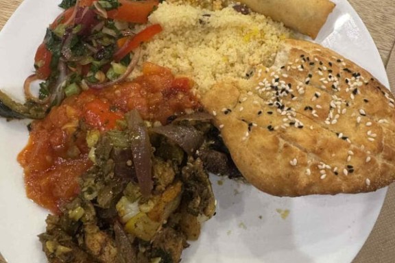 Plate with salad, couscous, flatbread, stew, and spring roll on a wooden table.