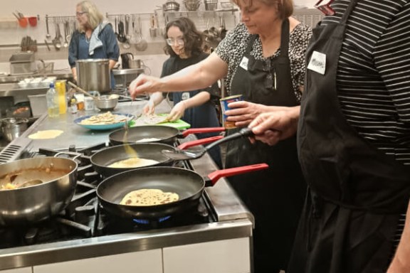 People cooking at a stove in a kitchen, wearing aprons and preparing food.