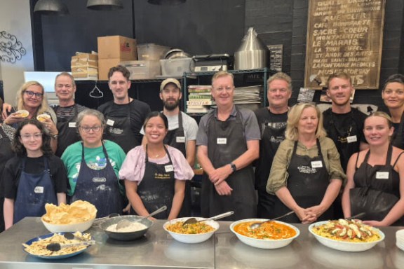 Group of people in aprons standing behind a table with various dishes.