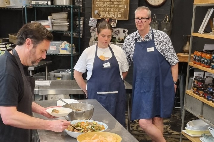 Three people cooking in a kitchen with prepared dishes on a metal table.