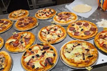 Several pizzas on plates with various toppings on a metal table.