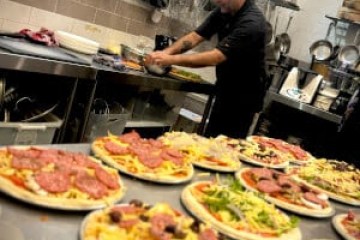 Chef preparing pizzas in a kitchen with various toppings on a counter.
