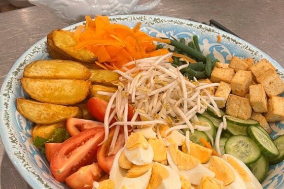 A plate of vegetables, boiled eggs, and tofu with peanut sauce in the background.