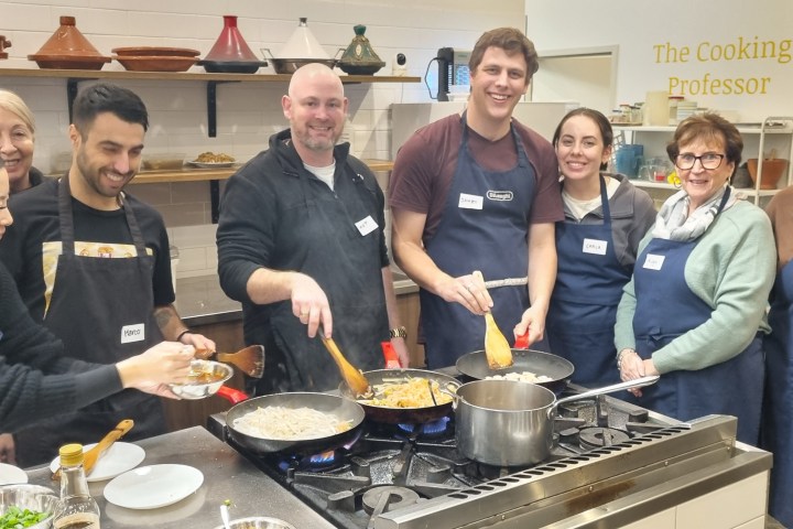 Group of people cooking at a class, wearing aprons, smiling at the camera.