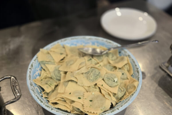 Plate of ravioli next to a pot on a metal surface.