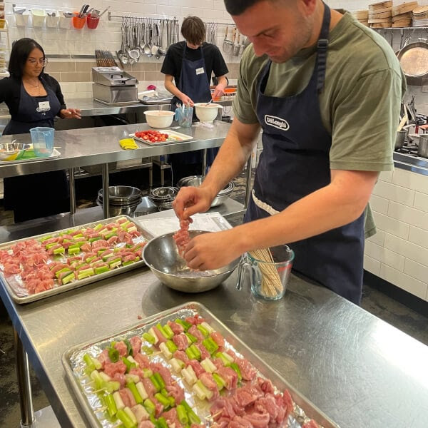 People preparing skewers with meat and vegetables in a kitchen setting.