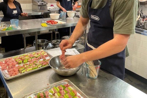 People preparing skewers with meat and vegetables in a kitchen setting.