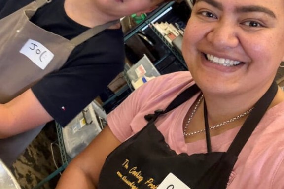 Two people smiling in aprons with name tags in a kitchen setting.