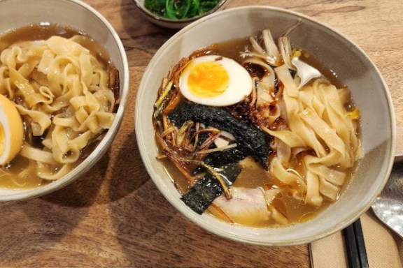 Two bowls of noodle soup with egg on wooden table, seaweed salad in a small bowl.