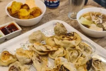 Table with dumplings, soup, plantain chips, and a ginger beer can.