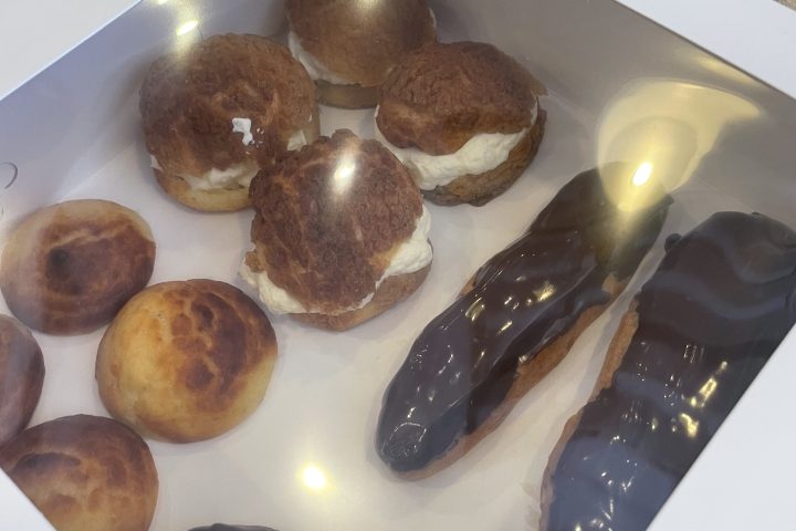 Box of assorted pastries including eclairs and cream puffs on a wooden table.