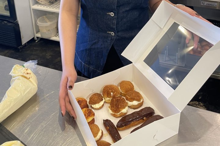 Person smiling and holding a box of pastries in a kitchen.