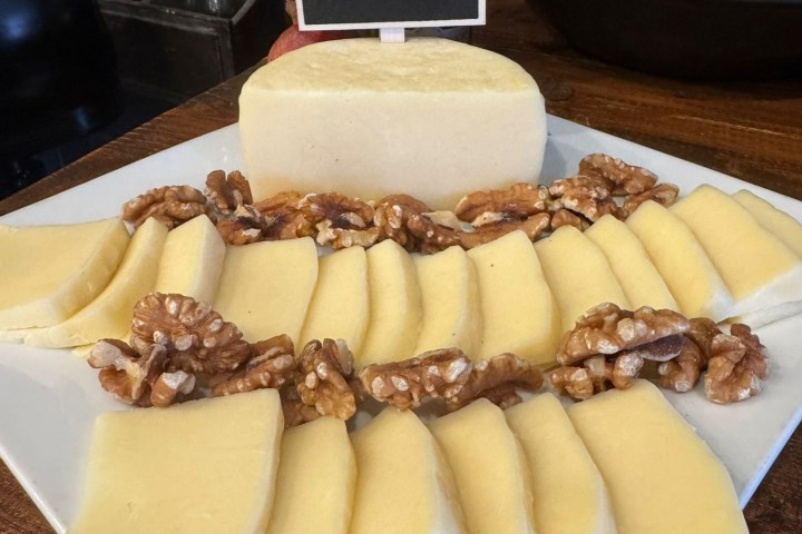 Sliced cheese and walnuts on a platter with a sign labeled 'Caciotta Plain'.