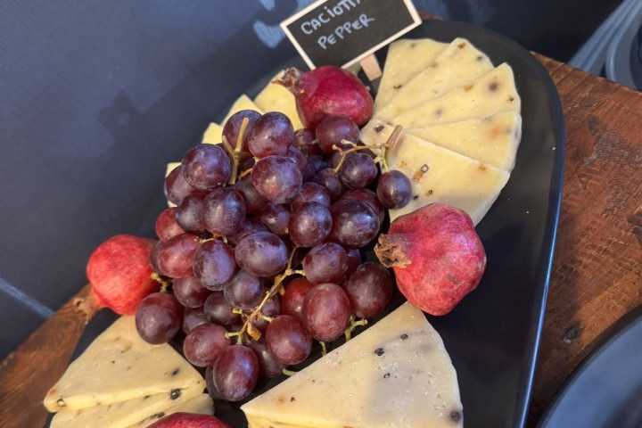 Cheese platter with grapes and pomegranates on a black plate.