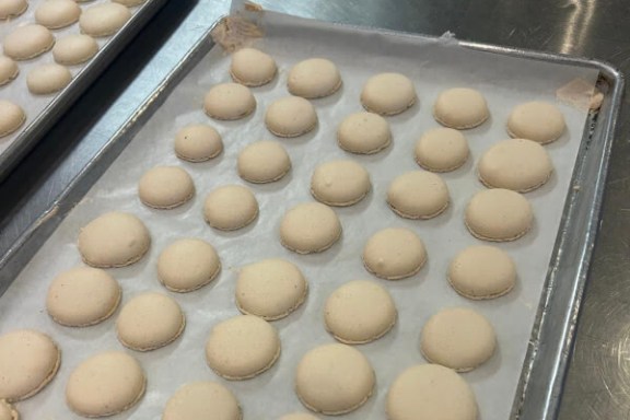 Unbaked white macaron shells on parchment-lined baking trays.