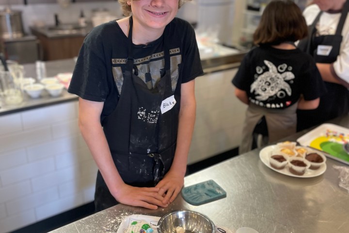 Child in kitchen wearing apron, standing by decorated tray with baking supplies.
