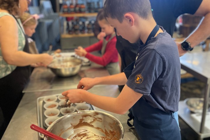 Kids and adults baking together, filling cupcake trays with batter in a kitchen.
