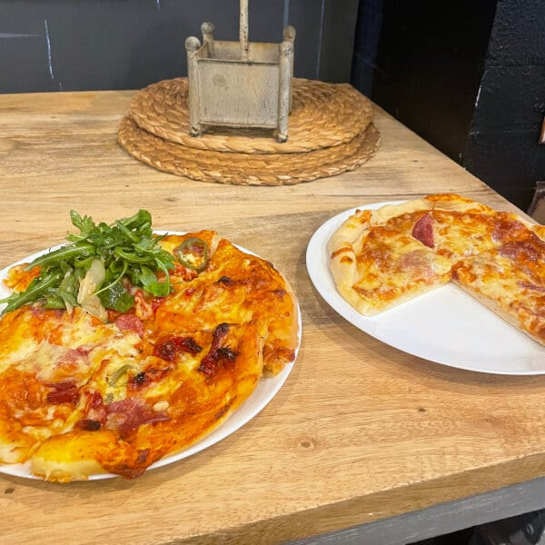 Two plates of pizza on a wooden table, one with arugula garnish.