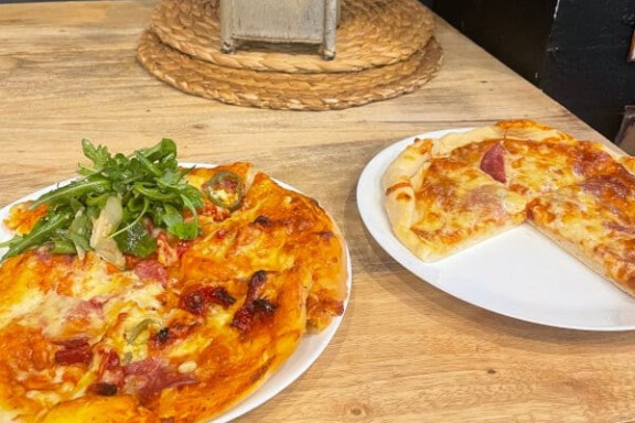 Two plates of pizza on a wooden table, one with arugula garnish.