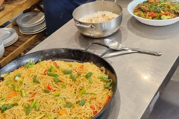 Dishes with noodles, rice, and stir-fried vegetables on a kitchen counter.