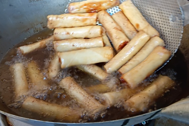 Spring rolls frying in a wok over a gas flame.